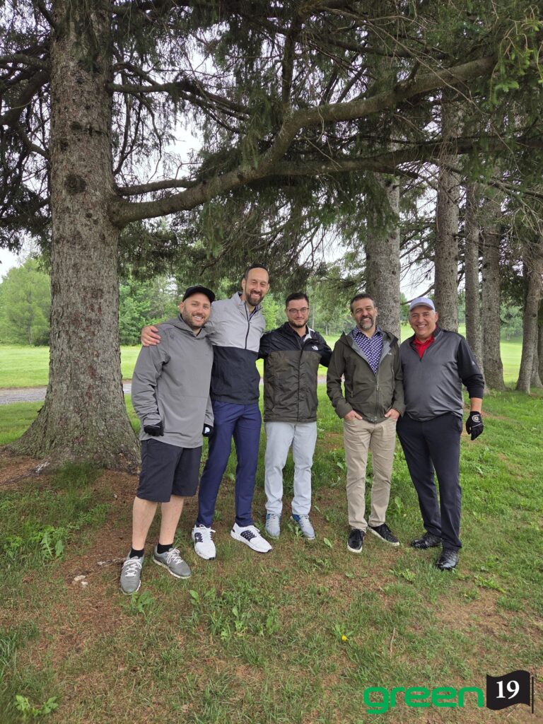 Cinq hommes souriants sous des arbres au golf