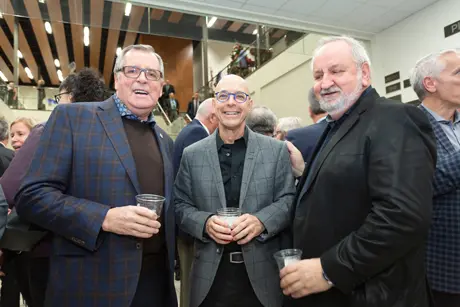 Trois hommes souriants lors d’un événement intérieur