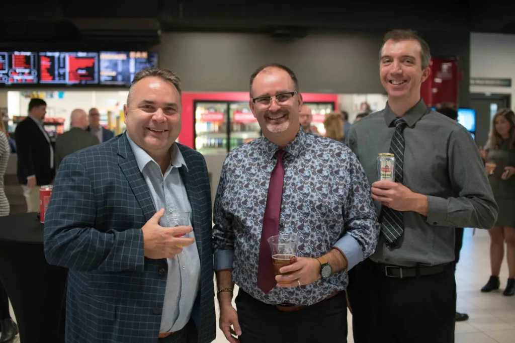 Trois hommes souriants lors d’un événement intérieur