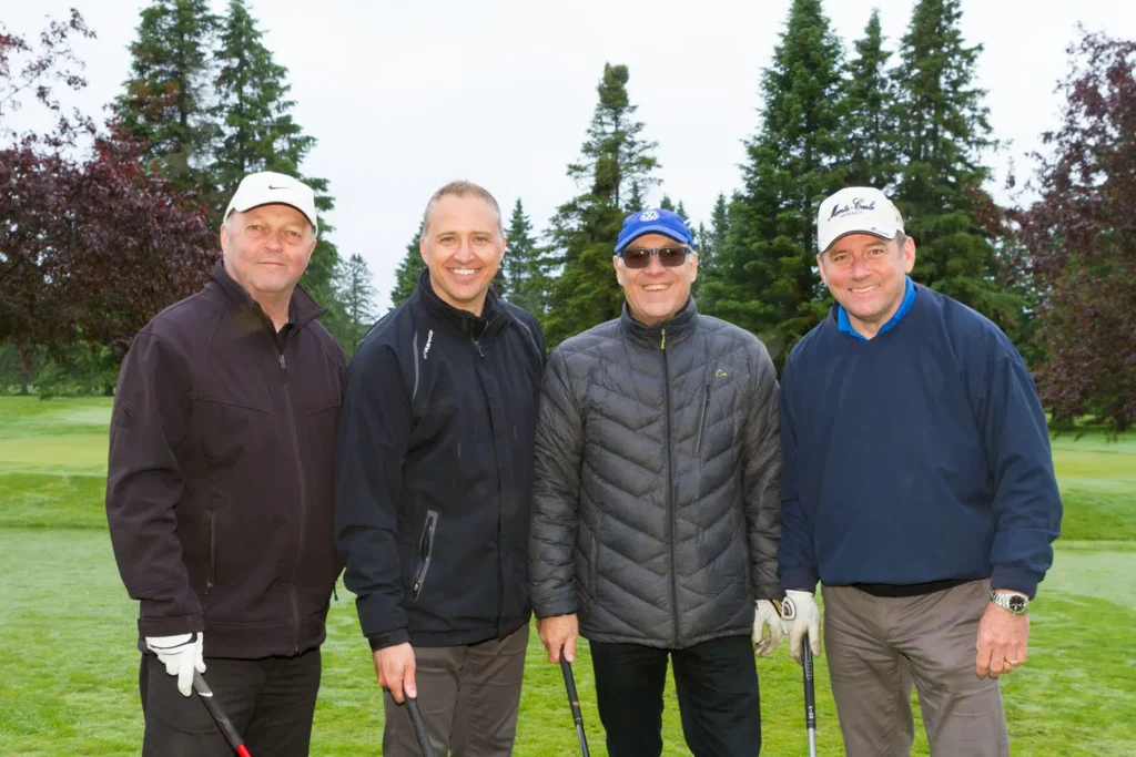 Quatre hommes souriants sur un terrain de golf