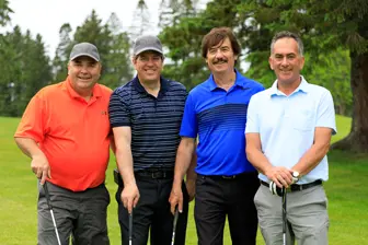 Quatre hommes souriants sur un terrain de golf