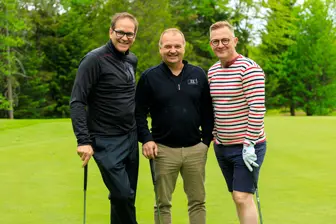 Trois hommes souriants sur un parcours de golf
