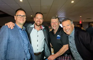 Quatre hommes souriants lors d’un événement en intérieur