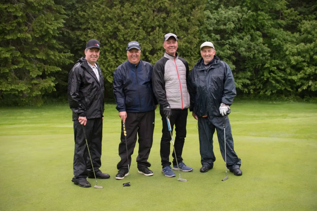 Quatre golfeurs souriants sur un green pluvieux