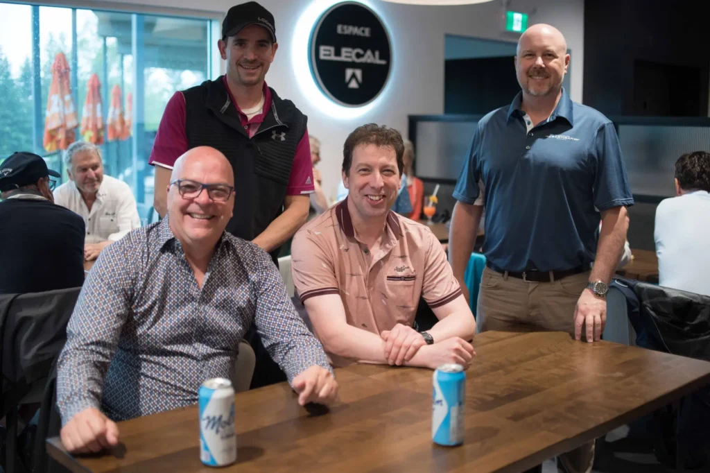 Quatre hommes souriants autour d’une table en intérieur
