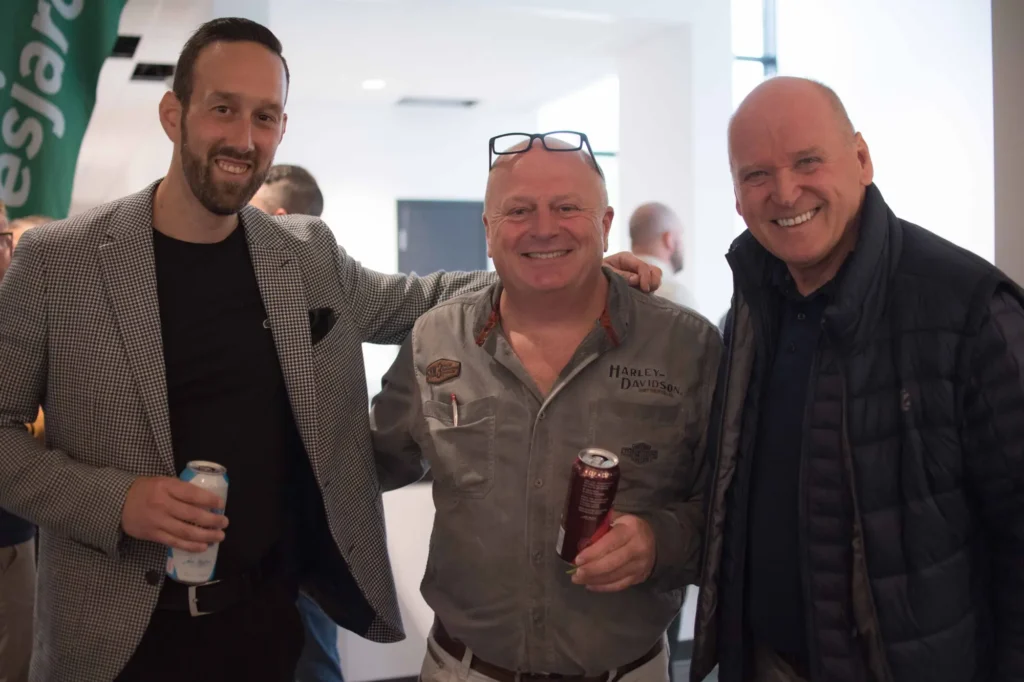 Trois hommes souriants lors d’un événement intérieur
