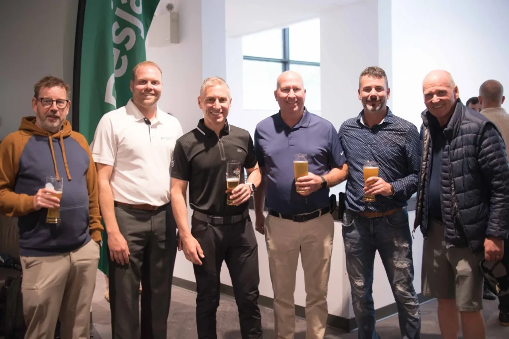 Six hommes souriants tenant des bières en intérieur