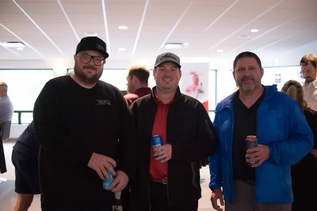 Trois hommes souriants lors d’un événement intérieur