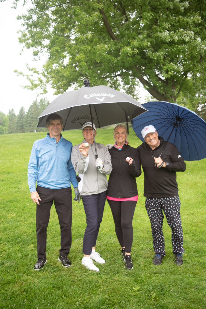 Quatre golfeurs souriants sous parapluies sur parcours